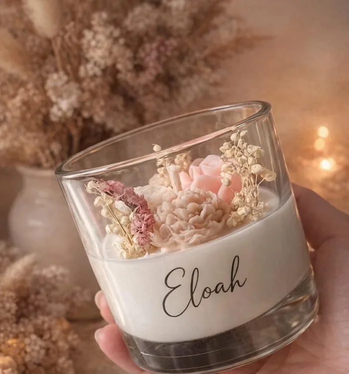 Vela artesanal de Eloah en vaso de vidrio con flores secas, sostenida en la mano